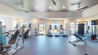 Located at 192 Little Nell Ln in Garner, NC, this single-story community clubhouse delivers a thoughtfully designed amenity space that blends modern aesthetics with practical functionality. The open-concept clubroom serves as the centerpiece, featuring light hardwood flooring, coffered ceilings with dark accent beams, and recessed lighting throughout. A bold dark shiplap accent wall anchors a lounge area furnished with comfortable seating arrangements, while large glass entry doors flood the space with natural light and offer views of the surrounding community.

The kitchen and bar area is a standout feature, showcasing navy cabinetry with brass hardware, a striking herringbone-patterned tile accent wall, a wall-mounted television, and a spacious island with bar seating illuminated by pendant lighting. An adjacent conference room offers a long wooden table, designer chandelier, and patterned window treatments, providing a polished setting for meetings. Café-style seating near floor-to-ceiling windows creates an ideal spot for casual gatherings.

The fitness center is generously sized, with high ceilings, ceiling fans, rubber flooring, and large mirrors. It is equipped with treadmills, stair climbers, free weights, cable machines, and weight benches, catering to a comprehensive range of workout needs.