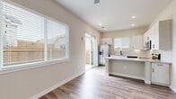 This single-story space is designed with a clean, modern aesthetic defined by a consistent warm neutral color palette and wood-look luxury vinyl plank flooring that runs throughout. The open-concept kitchen serves as a functional centerpiece, featuring white shaker cabinetry with dark hardware, a granite-topped island with breakfast bar seating, and a full suite of stainless steel appliances including a French door refrigerator, electric range, microwave, and dishwasher. Recessed lighting and a sliding glass door leading to a private outdoor area enhance the kitchen's bright, airy character. The living areas are generously proportioned, with a ceiling fan and light fixture adding both comfort and style. Multiple rooms throughout the unit are bathed in natural light from white-framed windows fitted with horizontal blinds. One room notably features elevated clerestory windows, adding architectural interest and additional light. The bathroom is finished with a white vanity, granite countertop, a large mirror, and matching wood-look flooring, maintaining design continuity. The exterior, visible in the 3D overview, reveals a compact, well-defined footprint with a small outdoor yard area.