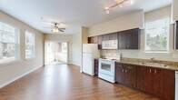 This thoughtfully designed single-floor unit offers an efficient and comfortable layout across its compact footprint. Rich hardwood-style flooring runs throughout, lending warmth and visual continuity to the entire space.

The open-concept kitchen and living area forms the heart of the unit. The kitchen is well-appointed with dark espresso cabinetry, granite countertops, a full suite of white appliances including a refrigerator, electric range, built-in microwave, and dishwasher, as well as a stainless steel sink beneath a window that invites natural light. Track lighting overhead ensures excellent task illumination.

The adjoining living area is generously proportioned for the overall footprint, featuring a ceiling fan with light fixture and multiple windows dressed with slatted blinds that fill the room with daylight and offer views of the surrounding exterior. A sliding glass door opens to a private balcony, seamlessly extending the living space outdoors.

A dedicated closet with a sliding door and built-in rod provides convenient storage near the entryway. The bathroom is clean and functional, featuring a full tub-shower combination with safety grab bars, neutral beige walls, and consistent hardwood-style flooring. The overall palette of warm beige tones and white trim creates a bright, welcoming ambiance throughout.