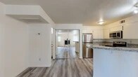 Located at 2020 Cheyenne in Modesto, California, this well-appointed single-floor residence offers a thoughtfully designed layout comprising a combined kitchen and living room, one bedroom, one bathroom, and a dedicated closet. Light-toned luxury vinyl plank flooring runs consistently throughout the home, contributing to a clean, cohesive aesthetic.

The open-concept kitchen is a functional highlight, featuring white cabinetry, granite-patterned countertops, a peninsula with bar seating potential, and a full suite of stainless steel appliances including a refrigerator, microwave, and electric range. A mirrored sliding door connects the kitchen area to the rest of the living space, enhancing the sense of openness and reflecting natural light.

The spacious living room is anchored by a stone-surround fireplace with a classic mantle, flanked by windows that bring in generous natural light and offer views of the surrounding greenery. A door leads directly to an outdoor area, further extending the living space.

The bedroom is a comfortable size and includes access to a dedicated closet. The bathroom is well-finished with a granite-top vanity, a mirrored medicine cabinet, and a shower-tub combination with sliding glass doors. Textured ceilings are present throughout, adding architectural character to this move-in-ready home.