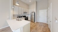 Located at 2051 Establishment Way in Charlotte, NC, this single-floor unit offers a thoughtfully designed layout with modern finishes throughout. The kitchen serves as a central highlight, featuring white shaker-style cabinetry extending to the ceiling, a classic subway tile backsplash, stainless steel appliances including a gas range, microwave, and refrigerator, and a peninsula with a white quartz countertop and undermount sink. Industrial-style pendant lighting adds a contemporary touch above the peninsula.

The living area is bright and open, with warm hardwood-style flooring and large windows that invite abundant natural light. Neutral beige tones on the walls create a clean, versatile backdrop throughout the space.

The bedroom is generously proportioned with high ceilings, soft carpeting, and windows fitted with white horizontal blinds. A connected walk-in closet and direct access to the bathroom add to its convenience.

The bathroom is designed with accessibility in mind, featuring stainless grab bars at the shower and throughout, a walk-in tiled shower with a handheld fixture, a wide single-sink vanity with a white countertop, and durable wood-look flooring. Safety alert fixtures are also present, reflecting a comprehensive approach to accessible living.