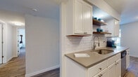 Located at 11141 Springhollow Rd in Oklahoma City, Oklahoma, this single-floor home offers a thoughtfully updated interior with modern finishes throughout. The galley-style kitchen is a standout feature, showcasing crisp white shaker cabinetry, warm wood open shelving, a classic white subway tile backsplash, taupe quartz countertops, a stainless steel undermount sink with a pull-down faucet, and stainless steel appliances including a refrigerator and dishwasher. Wood-look flooring runs throughout, adding warmth and continuity across the home. The living area is centered around a fireplace, creating an inviting focal point, and is complemented by a ceiling fan and a glass door that brings in natural light. The bedroom is generously proportioned, featuring wood-look tile flooring, a ceiling fan, and a window with blinds that allow for natural light. An adjacent bathroom provides white cabinetry with taupe countertops and a large vanity mirror. A dedicated office space offers room for a full desk setup and is brightened by a window with natural light. The overall aesthetic is clean, neutral, and modern, making this a well-appointed and functional single-level home.