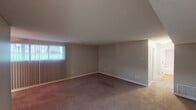 This single-floor residence offers a practical and comfortable layout across several well-defined living spaces. The galley-style kitchen is efficiently designed with warm wood cabinetry, granite-style countertops, a double stainless steel sink, and black appliances including a refrigerator and range. Light wood-style flooring runs underfoot, and ample upper and lower cabinet storage lines both sides of the kitchen, leading to an adjoining utility or storage area at the far end.

The living areas are generously proportioned, featuring plush carpet flooring in neutral tones, textured ceilings, and neutral-painted walls throughout. Vertical blinds on large windows allow for adjustable natural light, and a ceiling fan adds comfort to the main living space.

The bedroom is a standout feature, offering two side-by-side closets with built-in shelving and hanging rods, providing abundant storage. Carpet flooring continues here, and a window brings in natural light. An additional carpeted room serves well as a second bedroom or flex space, also benefiting from a window with outdoor views.

The bathroom is clean and functional, featuring a full soaking tub with white tile surround, a granite-topped vanity, wood-style flooring, and a wall-mounted mirror. The overall ambiance of the space is understated and move-in ready.
