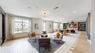 Located at 2880 Avila Cross Cir in Oviedo, Florida, this contemporary community living space is thoughtfully designed to accommodate a variety of social activities across a single, expansive floor. The interior is unified by light-toned wood-look tile flooring and crisp white walls, creating a bright and welcoming atmosphere throughout.

The main lounge area is anchored by a plush sectional sofa, a sculptural coffee table, and bold pendant lighting with an organic, branching design. Large windows dressed with linen drapes flood the space with natural light and offer views of the surrounding community. Adjacent to the lounge, a casual seating cluster features modern accent chairs in neutral tones accented with mustard yellow pillows, arranged around a patterned area rug.

The entertainment zone transitions seamlessly into a dedicated gaming area, complete with a poker table surrounded by rolling leather chairs, a pool table, and a shuffleboard table set on plush carpeting. A wall-mounted fireplace display and built-in shelving serve as a stylish focal point in this section. A work or dining area outfitted with a dark table and leather task chairs provides a more focused setting.

Geometric wall panels and contrasting gray accent walls add architectural interest throughout, while recessed lighting and designer pendants ensure a well-lit, polished ambiance. A sleekly finished stairwell with textured wallcovering connects to additional levels of the building.