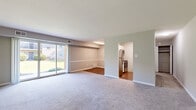 This single-floor residence offers a well-organized and functional layout designed for comfortable everyday living. The main living area is spacious and open, featuring soft carpet flooring that transitions into hardwood in the adjacent dining space. A large sliding glass door dominates one wall of the living room, flooding the interior with natural light and providing direct views of the surrounding green lawn and outdoor landscape. Neutral-toned walls throughout lend the space a clean, versatile aesthetic.

The kitchen is accessed through an arched entryway and is equipped with stainless steel appliances, including a refrigerator, electric range, and over-the-range microwave, all set against light-toned flooring and bright white walls.

The bedroom is generously sized with plush carpet flooring, soft gray walls, and two windows that invite ample natural light from multiple angles. A closet and direct access to the bathroom add to the room's practicality.

The bathroom features a white vanity with an integrated sink, a mirrored medicine cabinet, brushed nickel fixtures, and a full tub-shower combination framed by clean white tile surrounds. The overall ambiance of the space is bright, neutral, and move-in ready.
