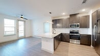 This well-designed two-bedroom, two-bathroom single-floor unit offers a functional and contemporary layout with thoughtful finishes throughout. The open-concept kitchen and living area serves as the heart of the space, featuring a central peninsula with granite countertops, an undermount sink with a matte black faucet, and pendant lighting above. The kitchen is equipped with stainless steel appliances—including a range, microwave, and dishwasher—dark espresso cabinetry, and a white subway tile backsplash. Light wood-tone flooring flows throughout the common areas, complementing the bright white walls and recessed lighting.

The living area benefits from natural light through multiple windows and a glass door leading to a private balcony, with a ceiling fan adding comfort. Both bedrooms are carpeted and include ceiling fans and dedicated closets with built-in shelving. The primary bedroom connects directly to its en-suite bathroom, which features a granite-topped vanity with dark cabinetry and a framed mirror. A second full bathroom serves the additional bedroom. Two closets provide ample storage throughout the unit.