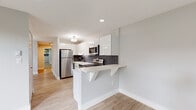Located at 392 State St in North Haven, Connecticut, this thoughtfully renovated single-floor unit blends modern design with functional living. The open-concept kitchen is a standout feature, showcasing high-gloss white cabinetry, stainless steel appliances including a refrigerator, electric range, microwave, and dishwasher, complemented by striking marble-veined countertops and a dark vertical tile backsplash. A built-in breakfast bar extends from the kitchen peninsula, offering a casual dining option that flows naturally into the open living area. Light wood-style flooring runs throughout the main living spaces, enhancing the bright, airy feel of the unit. The bathroom is tastefully updated with large-format grey wall tiles surrounding a full soaking tub and shower, a wall-mounted white vanity, and clean white tile flooring. The bedrooms are carpeted for comfort and feature generous closet space, including built-in shelving and large panel-door closets. Recessed lighting throughout provides consistent illumination, while windows allow natural light and outdoor views into the living areas. A well-organized hallway with additional storage closets adds to the unit's practical appeal. Overall, the space presents a clean, contemporary aesthetic with quality finishes throughout.