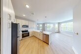Located at 700 N Second St in Brighton, MI, this thoughtfully designed single-floor residence offers three bedrooms, two bathrooms, and a dedicated laundry room. The open-concept kitchen and living area serves as the heart of the home, featuring light wood cabinetry, a herringbone tile backsplash, quartz countertops, a large peninsula with an undermount sink, and a full suite of stainless steel appliances. Pendant lighting and recessed fixtures illuminate the space, while expansive windows and a door to a private balcony flood the living area with natural light and offer pleasant outdoor views. Light hardwood flooring flows throughout the main living areas and hallways, complemented by plush carpet in the bedrooms. The primary bedroom includes a walk-in closet with wire shelving systems and an en-suite bathroom with a dual-sink vanity, quartz countertops, and a glass-enclosed walk-in shower. Additional bedrooms feature carpet flooring, natural light from well-placed windows, and closet access. The in-unit laundry room accommodates a full-sized washer and dryer. Neutral gray and beige tones throughout create a clean, modern aesthetic, making this a well-appointed and functional residence.