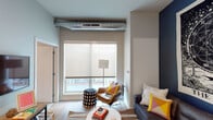 This single-floor unit offers a thoughtfully designed layout with multiple bedrooms, a living area, a kitchen, and two bathrooms. The living room makes a strong first impression with its industrial-modern aesthetic, featuring an exposed ductwork ceiling detail, light wood flooring, and a large window fitted with a roller shade that draws in natural light. A bold, dark accent wall provides a striking backdrop for the seating area, adding depth and personality to the space.

The kitchen is efficiently designed with white upper cabinetry, dark lower cabinets, white countertops, and a subway tile backsplash. Stainless steel appliances, including a refrigerator, range, microwave, and dishwasher, complete the functional setup.

The bedrooms are carpeted and finished with neutral gray walls, each featuring windows with roller shades. Several rooms include built-in desk areas or space for a study setup, making them well-suited for functional, everyday use.

Two bathrooms serve the unit; one features a dark vanity with a mirror and a shower-tub combo, while the second is similarly equipped with wood-look flooring, a white vanity, and a tub-shower combination. Both are clean and simply appointed.