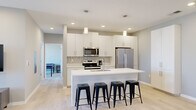 Located at 4500 E Third St in Bloomington, Indiana, this modern single-floor home offers three bedrooms and two bathrooms within a thoughtfully designed layout. The contemporary kitchen is a standout feature, showcasing white shaker cabinetry, a patterned tile backsplash, stainless steel appliances including a French door refrigerator and range, and a large island with a white countertop and seating for four. A tall pantry cabinet provides ample additional storage. Light wood-look flooring runs throughout, enhancing the clean, modern aesthetic. The living room is bright and welcoming, featuring recessed lighting, a sliding glass door, and a window that opens to a private balcony with views of the surrounding neighborhood. The bedrooms are comfortably scaled, with large windows that invite natural light and offer pleasant outdoor views. The bathrooms are finished in a neutral palette, featuring white vanities with light countertops, brushed nickel hardware, and a tub-shower combination. A hallway and closet round out the floor plan, providing practical everyday storage. The overall ambiance is clean, contemporary, and well-appointed, making this Bloomington home a functional and stylish living space.