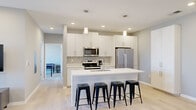 Located at 4500 E Third St in Bloomington, Indiana, this modern single-floor home offers three bedrooms and two bathrooms within a thoughtfully designed layout. The contemporary kitchen is a standout feature, showcasing white shaker cabinetry, a patterned tile backsplash, stainless steel appliances including a French door refrigerator and range, and a large island with a white countertop and seating for four. A tall pantry cabinet provides ample additional storage. Light wood-look flooring runs throughout, enhancing the clean, modern aesthetic. The living room is bright and welcoming, featuring recessed lighting, a sliding glass door, and a window that opens to a private balcony with views of the surrounding neighborhood. The bedrooms are comfortably scaled, with large windows that invite natural light and offer pleasant outdoor views. The bathrooms are finished in a neutral palette, featuring white vanities with light countertops, brushed nickel hardware, and a tub-shower combination. A hallway and closet round out the floor plan, providing practical everyday storage. The overall ambiance is clean, contemporary, and well-appointed, making this Bloomington home a functional and stylish living space.