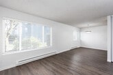 This single-floor unit is designed with a practical, straightforward layout that maximizes functionality across its key living spaces. The open living and dining area features smooth hardwood-style flooring, white walls, and a textured ceiling, creating a bright and airy atmosphere. A pendant light fixture anchors the dining area, while a window with blinds allows natural light to fill the space. A baseboard heating system runs along the exterior wall, providing efficient climate control.

The galley-style kitchen is efficiently organized with white shaker cabinetry lining both sides, offering ample upper and lower storage. Neutral laminate countertops provide generous prep space, complemented by a single-basin sink and white appliances including a range and refrigerator. Hardwood-style flooring continues throughout.

The bedrooms feature plush carpet and clean white walls. One bedroom includes a walk-in closet with built-in shelving and a hanging rod, while another offers a separate walk-in closet accessible through a paneled door. The full bathroom includes a tiled tub-shower combination, a toilet, and hardwood-style flooring, finished in a clean, minimal style consistent with the rest of the unit.