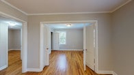 This single-floor, two-bedroom, one-bathroom residence offers a thoughtfully arranged layout finished with consistent warm-toned hardwood flooring throughout. Crown molding accents the ceilings in the main living areas, adding a classic architectural detail that elevates the overall aesthetic. Neutral gray walls provide a versatile backdrop across all rooms.

The living area is generously proportioned, featuring a ceiling fan with light fixture and multiple windows that allow natural light to fill the space. French-style double doors connect rooms, enhancing the open flow of the floor plan. Both bedrooms are well-sized; one features corner windows on two walls, maximizing natural light and outdoor views, while the second includes a standard closet with a rod and shelf for organized storage.

The kitchen is equipped with stainless steel appliances, including a gas range, over-the-range microwave, and dishwasher. White shaker-style cabinetry lines the upper and lower walls, complemented by a dark laminate countertop and a subtle tile backsplash. The bathroom features a full tub-shower combination with white tile surround, chrome fixtures, and a small window for natural ventilation. White trim and baseboards unify the design throughout the entire unit.