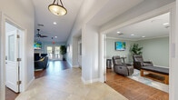 Located at 518 Lake Bridge Ln in Apopka, Florida, this single-floor community space offers a thoughtfully designed layout comprising two distinct living areas, a fully equipped kitchen, and a welcoming entrance. The entrance greets visitors with large-format tile flooring, recessed lighting, and a decorative pendant light, setting a polished tone for the rest of the space. The primary living room features rich hardwood flooring, vaulted ceilings with a ceiling fan, soft neutral walls, and a fireplace flanked by comfortable navy accent chairs and a leather sofa. French doors provide access to the outdoors, allowing natural light to fill the room. A wall-mounted flat-screen TV above the fireplace adds a modern amenity. The second living area, finished in soft sage green with crown molding and recessed lighting, offers a more relaxed atmosphere with plush recliner chairs, a wall-mounted TV, and an adjacent wet bar area for added convenience. The kitchen is outfitted with rich dark wood cabinetry, granite countertops, hardwood-style flooring, and black appliances, providing ample functionality. Together, these spaces create a cohesive, inviting environment well-suited for gathering and relaxation.