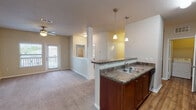 Located at 3502 Jenks Ave in Panama City, Florida, this single-story residence offers a well-designed, functional layout ideal for comfortable everyday living. The open-concept kitchen is a central highlight, featuring rich wood cabinetry, granite-style countertops, a double-basin sink, and a full suite of black appliances including a gas range, microwave, and refrigerator. Wood-look flooring runs throughout the kitchen, which flows seamlessly into the living area via a peninsula with pendant lighting overhead. Decorative columns with wainscoting detail define the transition between the kitchen and the carpeted living room, which benefits from a ceiling fan and access to an exterior door bringing in natural light. Bedrooms are generously sized with plush carpet, ceiling fans, and ample closet space — including a walk-in closet with wire shelving in one room. The bathroom is equipped with a dual-sink vanity, granite-style countertops, a large wall mirror, and wood-look flooring. A dedicated laundry area accommodates a full-sized washer and dryer side by side, with overhead shelving for added storage. The overall ambiance is clean, neutral, and move-in ready.