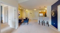 Located at 2011 Washington St in Newton, MA, this single-floor residence offers a well-organized layout that balances comfort and functionality throughout its living spaces. The open-concept living and dining area serves as the heart of the home, with plush carpeting underfoot and a bold accent wall in deep navy that creates a striking focal point. The dining space accommodates a full table and chairs, and flows seamlessly toward the kitchen and entry foyer. The kitchen features warm wood cabinetry, granite countertops, tile flooring, and stainless steel appliances, including a range and dishwasher. A breakfast bar with pendant lighting provides additional seating and connects the kitchen to the main living area. The two bedrooms are carpeted and generously proportioned, each featuring large windows that invite natural light and offer views of the surrounding greenery. Accent walls in soft green and muted teal lend each room a distinct character. Both bathrooms are finished with granite-topped vanities, wood cabinetry, and tile flooring, with one bathroom featuring a full tub-shower combination. Throughout the residence, neutral tones and quality finishes create a cohesive and welcoming ambiance well-suited to everyday living in the heart of Newton.