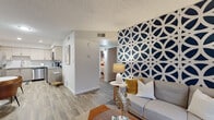 This thoughtfully designed single-floor residence makes a strong first impression with its living room's bold navy and white geometric feature wall, which serves as a striking focal point against wood-look flooring and a textured ceiling. The space is furnished with a comfortable sofa, mid-century modern accent chairs, and warm-toned accessories that create an inviting yet design-forward atmosphere. Natural light filters through large windows dressed with layered blinds and curtains, enhancing the open, airy feel throughout.

The kitchen is outfitted with light wood cabinetry, granite-look countertops, and a full suite of stainless steel appliances including a dishwasher, range, and built-in microwave — offering both style and practicality for everyday living.

Two well-proportioned bedrooms each feature their own navy accent walls, wood-look flooring, and large windows that allow generous natural light. The rooms provide comfortable retreats with ample space for king-sized furnishings.

The bathroom is clean and contemporary, featuring a light wood vanity with a white countertop, a tub-shower combination, and wood-tile flooring accented with decorative shelving.

A dedicated laundry area with full-size side-by-side washer and dryer units, topped by a storage shelf, adds exceptional convenience to this well-appointed residence.