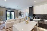 Located at 8448 Delmar Blvd in University City, MO, this thoughtfully designed 2-bedroom, 2-bathroom residence offers a sleek, contemporary aesthetic across a single floor. The open-concept kitchen and living area serves as the heart of the home, featuring a striking two-tone kitchen with dark cabinetry contrasted by crisp white upper cabinets and countertops, a dark tile backsplash, stainless steel appliances, and a central island with seating. The living room is bright and airy, with light wood flooring, recessed lighting, and black French doors that open to a private balcony, bringing in abundant natural light and outdoor views. Both bedrooms are carpeted and well-lit with large windows that frame greenery and city views. The primary bedroom is generously sized, offering a comfortable retreat. The two bathrooms are finished with a clean, modern palette — one featuring dramatic dark marble-look tile flooring, a white floating vanity, and matte black fixtures for a bold, refined look. Hallways connect the spaces efficiently, and a dedicated closet adds practical storage. The overall ambiance is polished and contemporary, with a neutral color palette and high-end finishes throughout.