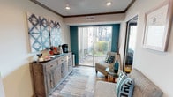 This leasing center is thoughtfully designed to create a professional yet inviting atmosphere for visitors. The single-floor layout features wood-look flooring throughout, dark crown molding, and recessed lighting that lend a cohesive, polished aesthetic across all areas.

The welcoming lounge area showcases a bold teal accent wall and large sliding glass doors that flood the space with natural light and offer views of the landscaped outdoor surroundings. A rustic wooden sideboard, complete with a coffee station, serves as a hospitality focal point, complemented by abstract wall art and comfortable seating arranged around a glass accent table.

Private office areas are furnished with spacious L-shaped desks and ergonomic seating, providing a functional workspace for leasing staff. Framed artwork and decorative wall sconces add a refined touch, while large windows dressed in patterned drapes allow ample natural light. One office overlooks a fitness center through glass-paneled doors, offering convenient visibility to that amenity.

The main entrance features a glass door with patterned curtains and a view of the parking area, ensuring easy access and visibility from the exterior. Overall, the leasing center strikes a balance between approachable comfort and professional functionality, making it an ideal first impression for the community.