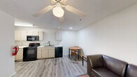Located at 101 Legacy Ter in Chapel Hill, NC, this one-bedroom, one-bathroom unit offers a practical and functional layout across a single floor. The open-concept living area flows seamlessly into the kitchen and dining space, all finished with light wood-look vinyl flooring. The kitchen is well-equipped with black appliances including a refrigerator, electric range, microwave, and dishwasher, complemented by light wood cabinetry and a double-basin sink with ample counter space. A dedicated dining nook with room for a small table sits adjacent to the kitchen. The living area features a ceiling fan with light fixture, adding both comfort and illumination. The bedroom is carpeted for warmth and comfort, also outfitted with a ceiling fan, and connects directly to a spacious walk-in closet with built-in shelving and dresser space. A stacked washer and dryer unit is conveniently tucked into a closet within the bedroom area, offering in-unit laundry. The bathroom includes a clean, full-size tub and shower combination with white surround. Neutral wall tones and textured ceilings run throughout, creating a cohesive and low-maintenance living environment well-suited for individuals or couples.