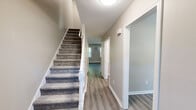 Located at 241 New State Rd in Manchester, CT, this multi-floor home offers a well-organized layout across three levels, including a finished basement. The main living level features warm-toned walls, durable luxury vinyl plank flooring, and a bright dining room anchored by a stylish multi-bulb chandelier and a large window that invites natural light. The galley-style kitchen is a standout, outfitted with crisp white shaker cabinetry, quartz countertops, a matte black sink fixture, and a full suite of stainless steel appliances. A carpeted staircase with white balustrades connects the floors, flanked by a clean hallway with additional closet access. Upstairs, the two bedrooms feature plush carpeting, neutral walls, and ample closet space, including sliding-door closets. The generously sized primary bedroom also includes a wall-unit air conditioner and baseboard heating. Both bathrooms are finished with white vanities, tile-surround tub-shower combos, and wood-look flooring. The unfinished basement provides considerable open space with concrete floors, exposed joists, and visible utility infrastructure, making it well-suited for storage or future finishing. With five closets throughout, this home offers practical storage at every turn.