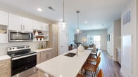 This single-floor residence at 1001 Compass Way in Newark, Delaware, presents a thoughtfully designed open-concept layout that seamlessly connects the kitchen, dining, and living areas. The kitchen serves as a central highlight, featuring a two-tone cabinetry scheme that pairs crisp white upper cabinets with warm natural wood lower cabinets. A generous island with a white quartz countertop and undermount sink anchors the space, illuminated by a pair of glass pendant lights. Stainless steel appliances, including a refrigerator, range, and microwave, complement the clean aesthetic, while light wood-tone flooring extends throughout the main living areas.

The living room offers a welcoming atmosphere with neutral tones and direct access to a private balcony through sliding glass doors, allowing natural light to flow in. The bedroom features plush carpeting, large windows with views of the surrounding community, and ample space for full-sized furnishings. The en-suite bathroom is finished with large-format tile flooring, a glass-enclosed shower, and a walk-in closet, maintaining the residence's consistent modern and clean design sensibility throughout.