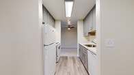Located at 9300 W Mall Dr in Everett, Washington, this single-floor unit offers four bedrooms and two bathrooms with a thoughtfully laid-out floor plan. The galley-style kitchen is a standout feature, lined on both sides with soft gray shaker cabinetry extending floor to ceiling, providing generous storage. Marble-patterned countertops complement the cabinetry, and the kitchen is equipped with a full-size refrigerator, electric range, and dishwasher. A skylight-style overhead fixture and ceiling fan at the adjoining hallway brighten the space, while light wood-look flooring runs throughout the kitchen. The living room is carpeted and generously proportioned, featuring a sliding glass door that opens to an outdoor area, allowing natural light to filter in. Each of the four bedrooms is finished with plush carpeting and neutral wall tones; the bedrooms feature windows with views of lush greenery, contributing to a calm, natural ambiance. The primary bedroom offers a comfortable footprint with closet access. Both bathrooms are finished with wood-look tile flooring and gray vanity cabinetry with stone-topped counters; one bathroom includes a full soaking tub and shower combination. A central hallway connects the living areas to the bedrooms, providing a practical and organized flow throughout the home.
