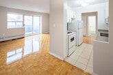 This well-organized one-bedroom, one-bathroom unit at 6 14th St in Toronto's New Toronto neighbourhood offers a thoughtfully laid-out single-floor plan. The living room is the largest area of the unit, featuring warm parquet flooring in a classic basket-weave pattern that extends throughout the space. Large sliding glass doors lead to a balcony, allowing natural light to fill the room, while a baseboard heating unit runs along the exterior wall. A second window provides additional light from another angle, enhancing the open feel of the space.

The kitchen is efficiently designed with white cabinetry extending to the ceiling for ample storage, neutral stone-toned laminate countertops, a subtle tile backsplash, and standard white appliances including a refrigerator and electric stove. A pendant light fixture adds a finishing touch.

The bedroom is a comfortable size, featuring the same parquet flooring and a built-in closet with sliding doors, along with an additional secondary closet for extra storage. Neutral grey walls throughout the unit create a clean, cohesive aesthetic.

The bathroom includes a full bathtub and shower combination with white tile surround, maintaining the unit's consistent, clean finish. A hallway connects all rooms, completing the functional layout.