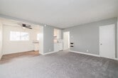 Located at 1321 W Rosecrans Ave in Gardena, California, this single-floor unit offers a clean, functional layout with a neutral color palette throughout. The living area is generously sized, featuring plush gray carpeting, a textured ceiling, and multiple windows dressed with vertical blinds that allow ample natural light to fill the space. A ceiling fan adds comfort and airflow to the room. The open layout connects the living area seamlessly to the kitchen, which is outfitted with white cabinetry, a light gray subway tile backsplash, dark countertops, a double basin sink, and a white electric range. Light wood-style flooring and track lighting give the kitchen a bright, practical feel. The bedrooms are carpeted and well-lit, each featuring ceiling fans, windows with vertical blinds, and mirrored sliding closet doors that enhance the sense of space. One room includes a wall-mounted heating unit and exterior-facing window with security bars. The bathroom is finished in a crisp all-white design, complete with a vanity featuring white cabinetry and brushed nickel hardware, a mirrored medicine cabinet, and a tub-shower combination with tile surround. Wood-look flooring ties the bathroom together with a clean, modern aesthetic.