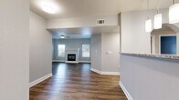 Located at 6010 Prairie Hills View in Colorado Springs, CO, this well-appointed 3-bedroom, 2-bathroom single-floor home offers a thoughtfully designed open-concept layout. The combined kitchen and living area serves as the heart of the home, anchored by rich wood-look flooring, a sleek fireplace with a white surround, a ceiling fan, and French doors that invite natural light and outdoor views. The kitchen is outfitted with crisp white shaker cabinets, granite countertops, stainless steel appliances including a range, microwave, refrigerator, and dishwasher, plus pendant lighting over the breakfast bar. Both bathrooms feature granite-topped white vanities, wood-look flooring, and tub/shower combinations. The three bedrooms offer plush carpeting, ceiling fans, and ample closet space, with five closets distributed throughout the home. The primary bedroom provides a comfortable and private retreat. Additional spaces include a dedicated laundry room and a utility room. Neutral gray tones on the walls complement the warm flooring throughout, creating a cohesive and modern aesthetic. The home also includes abundant storage across its five closets, rounding out a practical and attractive living space.