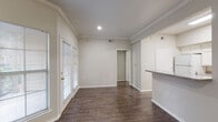 Located at 2821 Turnberry Dr in Arlington, Texas, this single-story unit offers a well-organized layout with a neutral color palette and a blend of practical finishes throughout. The living area is anchored by rich, dark hardwood-style flooring that extends through the main living spaces, complemented by crown molding and recessed lighting that enhance the clean, finished look of the interior. Natural light filters in through blinds-covered windows and a set of French doors, adding brightness to the open feel of the main area.

The kitchen is positioned adjacent to the living space and features a pass-through counter with granite-look surfaces, white cabinetry offering generous storage, and white appliances including a range and built-in microwave. A dedicated dining or flex area sits nearby, complete with built-in shelving along one wall, providing functional display and storage options.

The bedrooms are carpeted for comfort and include windows with outdoor views and closet space. One bedroom features a walk-in closet, while the bathroom presents a wide vanity with a granite-look countertop, white cabinetry, and a well-lit mirror. The overall ambiance is clean, neutral, and move-in ready.