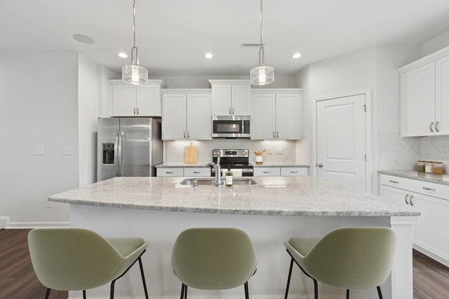 Upgrade Package kitchen with white cabinetry, designer tile backsplash and undercabinet lighting, and granite countertops - Avalon Townhome Collection Brier Creek