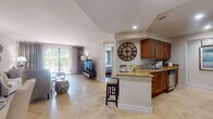 Located at 340 W Palmetto Park Rd in Boca Raton, Florida, this single-floor residence offers a thoughtfully designed open-concept layout that connects the living, dining, and kitchen areas into one cohesive space. Travertine tile flooring flows consistently throughout the main living areas, lending a warm, upscale feel to the interior.

The kitchen is well-appointed with rich wood cabinetry, granite countertops, stainless steel appliances including a full-size refrigerator and range, and a peninsula with bar seating that serves as both a functional workspace and a casual dining spot. A decorative oversized wall clock adds a distinctive design element to the kitchen area.

The living room is bright and inviting, featuring large sliding glass doors that provide direct outdoor access and frame lush greenery beyond, drawing in generous natural light. The dining area sits nearby and includes a closet for additional storage.

The primary bedroom features warm hardwood-style flooring, a sliding glass door with outdoor views, and ample natural light. A second bedroom offers a serene, well-appointed retreat. Two bathrooms serve the residence — one with a soaking tub and large-format tile surround, and another featuring a distinctive soaking tub framed by ornate arched mirrors, creating an elegant, spa-like atmosphere.