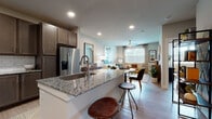 This single-floor residence is designed with an open-concept layout that seamlessly connects the kitchen, dining, and living areas. The kitchen serves as the centerpiece, featuring a large granite-topped island with an undermount sink and bar seating for casual dining. Dark taupe cabinetry with brushed nickel hardware pairs with a classic white subway tile backsplash, while stainless steel appliances—including a French door refrigerator with ice and water dispenser, electric range, and built-in microwave—complete the well-equipped space. Light wood-tone flooring runs throughout, unifying the open floor plan.

The living area offers a bright, welcoming atmosphere, illuminated by a broad window with shuttered blinds that invites natural light. A ceiling fan adds comfort, while neutral walls provide a versatile backdrop. The dining area provides an intimate space adjacent to both the kitchen and living room for easy entertaining.

The bathroom features a soaking tub with white subway tile surround and wood-look flooring. A spacious walk-in closet connects directly to the bathroom, offering ample built-in shelving and hanging rods for organized storage. Recessed lighting throughout the unit ensures consistent, modern illumination.