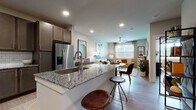 This single-floor residence is designed with an open-concept layout that seamlessly connects the kitchen, dining, and living areas. The kitchen serves as the centerpiece, featuring a large granite-topped island with an undermount sink and bar seating for casual dining. Dark taupe cabinetry with brushed nickel hardware pairs with a classic white subway tile backsplash, while stainless steel appliances—including a French door refrigerator with ice and water dispenser, electric range, and built-in microwave—complete the well-equipped space. Light wood-tone flooring runs throughout, unifying the open floor plan.

The living area offers a bright, welcoming atmosphere, illuminated by a broad window with shuttered blinds that invites natural light. A ceiling fan adds comfort, while neutral walls provide a versatile backdrop. The dining area provides an intimate space adjacent to both the kitchen and living room for easy entertaining.

The bathroom features a soaking tub with white subway tile surround and wood-look flooring. A spacious walk-in closet connects directly to the bathroom, offering ample built-in shelving and hanging rods for organized storage. Recessed lighting throughout the unit ensures consistent, modern illumination.