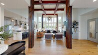 Located in Baton Rouge, Louisiana, this single-story clubhouse is a thoughtfully designed community gathering space that masterfully blends rustic character with modern refinement. The grand main living area commands attention with its soaring double-height ceilings framed by rich, reclaimed wood box beams and dramatic structural columns. Expansive floor-to-ceiling windows flood the space with natural light while offering unobstructed views of the surrounding outdoor amenities, including a pergola and manicured grounds. Wide-plank hardwood flooring flows seamlessly throughout, tying together each distinct zone of the clubhouse. The fully appointed kitchen features soft gray shaker cabinetry, a striking quartz waterfall island with bar seating, stainless steel appliances, a professional-grade range hood, and industrial-style pendant lighting — equally suited for casual gatherings or catered events. A welcoming entry foyer with a live-edge communal table and barn door detail provides a stylish transition into the main space. Additional lounge areas offer cozy, intimate settings with curated décor, arched windows, and ample natural light. A fitness area is also visible within the open layout. Throughout, the design strikes a balance between warmth and sophistication, making this clubhouse an exceptional amenity space.