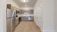 This single-story home features a thoughtfully designed layout accommodating three bedrooms, two full bathrooms, and a combined kitchen and living area, all connected by multiple hallways and complemented by two closets and a dedicated laundry room. Light-toned luxury vinyl plank flooring runs consistently throughout the home, contributing to a clean, cohesive aesthetic.

The open kitchen is well-equipped with stainless steel appliances — including a refrigerator, electric range, over-the-range microwave, and dishwasher — paired with taupe shaker-style cabinetry and light stone-look countertops. The adjoining living area benefits from natural light provided by a set of glass French doors, creating a bright and welcoming atmosphere.

The bedrooms are bright and simply designed, with neutral walls and windows fitted with blinds. The primary bedroom offers a comfortable amount of space. Both bathrooms feature wood-toned vanities, large mirrors, and full tub-shower combinations with curved curtain rods. The dedicated laundry room houses a full-size top-loading washer and dryer with overhead shelving, offering convenient in-home laundry facilities.