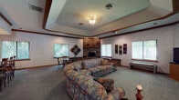Located at 1515 Steffen Ct in Fort Wright, Kentucky, this single-floor space is designed to accommodate gatherings and social events with a thoughtful, functional layout. The centerpiece of the space is a generous lounge area featuring a full brick fireplace with a raised hearth and built-in brick bench seating, creating a warm and inviting focal point. A tray ceiling with a ceiling fan adds architectural interest overhead, while multiple large windows with vertical blinds allow natural light to filter in and offer views of the surrounding greenery. The lounge comfortably accommodates ample seating and includes a dedicated dining area with a bar-height counter and decorative pendant lighting. The galley-style kitchen is fully equipped with dark wood cabinetry, a range, refrigerator, dishwasher, and double sink — well-suited for catering or event support. Textured wallcoverings, wood crown molding, and decorative wall art contribute to a cohesive, classic interior aesthetic throughout. The overall ambiance is comfortable and versatile, making the space well-suited for community gatherings, private events, or social functions.