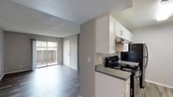 This single-floor residence offers a clean, modern aesthetic defined by neutral gray tones, durable wood-look flooring, and plush carpet in the sleeping areas. The open-concept layout connects the kitchen directly to the living area, creating a seamless flow throughout the main living space. A sliding glass door leads to a private outdoor patio, allowing natural light to fill the room.

The kitchen is efficiently designed with crisp white cabinetry, dark granite-style countertops, a stainless steel sink, and black appliances including an electric range and dishwasher. Under-cabinet ventilation and ample upper and lower storage make this a highly functional cooking space.

The living area features wood-look vinyl flooring and a textured ceiling, with the sliding patio door serving as both a light source and outdoor access point. The entry area includes a front door with adjacent closet storage and opens to additional interior rooms.

The bedrooms are finished with soft carpet and windows that bring in outdoor views and natural light. The primary bedroom features an ensuite vanity area with a sink and mirror, providing added convenience. The full bathroom includes a white soaking tub with a curved shower rod and chrome fixtures. A laundry area is also present within the unit, adding everyday practicality to this thoughtfully laid-out home.