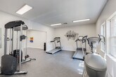 Located at 2500 Dauphinwood Dr in Mobile, Alabama, this single-floor fitness facility is purpose-built to support a comprehensive exercise experience. The entry features warm, classic brick-tile flooring and interior windows that offer a clear view into the adjacent spaces, creating an open and inviting first impression.

The main workout area is generously proportioned, finished with durable concrete flooring and illuminated by recessed fluorescent panel lighting throughout. This space accommodates multiple cardio machines, including treadmills and an elliptical trainer, as well as a multi-function cable weight machine and a wall-mounted rack of colorful resistance bands. A motivational fitness-themed word art mural serves as a visual focal point on one wall, reinforcing the space's dedicated athletic purpose. Natural light enters through a pair of windows along one wall, complementing the bright overhead lighting.

An adjoining multipurpose room offers a clean, open layout with crisp white walls, concrete flooring, and built-in wall-mounted hooks — ideal for stretching, yoga, group classes, or flexible training use. The space is well-ventilated with visible HVAC supply vents.

Throughout, the facility maintains a clean, minimalist aesthetic with white walls and a neutral color palette, creating a focused and functional environment well suited for fitness and wellness activities.