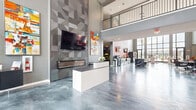 Located at 2101 Railway Ln. in Marysville, Ohio, this single-floor community clubhouse is a visually dynamic space designed to impress. The defining architectural feature is the stunning polished epoxy flooring with a swirling marble-like pattern in silver and blue tones, which flows seamlessly throughout the entire space, reflecting light and amplifying the sense of openness.

The grand entry lobby greets visitors with soaring ceilings, floor-to-ceiling glass walls, and an elegant sculptural chandelier that anchors the space overhead. Natural light pours in through expansive windows, offering clear views of the surrounding residential community.

The main lounge area is generously proportioned and divided into multiple seating zones, each thoughtfully furnished with plush grey velvet sofas, sleek chrome-accented chairs, bold red accent furniture, and contemporary round tables. Vibrant large-format abstract artwork adorns the grey walls throughout, infusing the space with energy and color.

A café-style bar area is equipped with beverage stations and display refrigerators, adjacent to high-top seating with red chairs. A geometric-tiled accent wall frames a mounted flat-screen television and a sleek fireplace console, adding architectural texture. Additional amenities visible include a billiards table, providing a well-rounded recreational atmosphere throughout this expansive, design-forward community space.