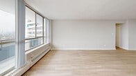 Located in Thorncliffe Park, Toronto, this generously sized two-bedroom, one-bathroom unit offers a bright and functional layout finished with light-toned hardwood flooring throughout. The expansive living area is a standout feature, bathed in natural light through floor-to-ceiling windows that frame sweeping panoramic views of the surrounding cityscape and beyond. Baseboard heating runs along the window walls, ensuring comfort year-round.

The primary bedroom is a well-proportioned retreat, benefiting from its own large window wall with balcony access and far-reaching views. The second bedroom is equally bright, featuring its own window and light-filled ambiance. A dedicated walk-in closet provides generous storage capacity with built-in shelving on multiple walls.

The kitchen is designed for efficiency, featuring white cabinetry, a double sink, laminate countertops, tile backsplash, and white appliances including a refrigerator and electric range. The bathroom is appointed with a white vanity, large mirror, and classic mosaic tile flooring. A hallway connects the living spaces seamlessly, completing this clean, move-in-ready unit ideal for those seeking comfortable urban living in Toronto.