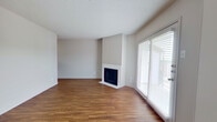 This single-floor space is designed with a clean, neutral aesthetic throughout, offering a functional and comfortable layout. The living area serves as the central gathering space, featuring warm wood-style flooring, a white-surround fireplace as a focal point, and a large sliding glass door fitted with horizontal blinds that allows generous natural light to fill the room. A textured ceiling adds subtle character overhead.

A hallway connects the living area to the remaining rooms, with textured walls lending a tactile contrast to the otherwise smooth finishes. The galley-style kitchen is efficiently arranged, featuring gray cabinetry on both sides, a stainless steel sink, matching countertops, and black appliances including a range and dishwasher. Wood-style flooring continues seamlessly from the living spaces into the kitchen.

The bedrooms are well-proportioned, each finished with the same wood-style flooring and neutral walls. Windows fitted with horizontal blinds provide natural light and privacy in equal measure. The bathroom includes a full-size tub and shower combination with white tile surround and chrome fixtures, maintaining the clean, understated style present throughout the entire space.