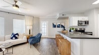 This single-floor residence offers a thoughtfully designed open-concept layout that seamlessly connects the living, dining, and kitchen areas. The living room features crown molding, wood-look flooring, abundant natural light from multiple windows, and a ceiling fan, creating a bright and comfortable gathering space. A glass-paneled door provides additional light and easy access to the outdoors. The adjacent dining nook offers an intimate setting with generous window exposure. The kitchen is well-equipped with white shaker cabinetry, dark countertops, stainless steel appliances, and a breakfast bar with seating — ideal for both cooking and casual dining. Two bedrooms are present, each with ceiling fans, wood-look flooring, and large windows. The primary bedroom includes sliding door access to a private balcony. The primary bathroom features a walk-in closet, vanity with dark countertops, and a glass-enclosed shower. A second full bathroom includes a tub-shower combination and a well-appointed vanity. A dedicated in-unit laundry area with a full-size washer and dryer adds convenience. Throughout, the neutral color palette and consistent flooring lend the space a cohesive, modern aesthetic.