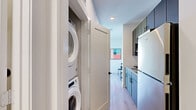 Located at 701 Richmond Ave in Houston's vibrant Montrose neighborhood, this efficiently designed studio offers a thoughtful single-floor layout that maximizes every square foot. The combined kitchen and living area forms the heart of the space, featuring light wood-style flooring that runs throughout and large windows that invite abundant natural light and outdoor views. The living area accommodates a clear separation between sleeping and lounge zones, aided by a freestanding open shelving unit that doubles as a room divider and media console — a smart design solution for open-plan living.

The kitchen is well-appointed with granite countertops, dark cabinetry, a tile backsplash, an electric cooktop, built-in microwave, and full-size refrigerator — providing a complete cooking setup within a compact galley-style footprint. A dedicated closet along the kitchen corridor houses a stacked washer and dryer, adding valuable in-unit laundry convenience.

The bathroom features white cabinetry with granite countertops, an undermount sink, black hardware accents, and light wood flooring that ties seamlessly to the rest of the unit. Clean white walls and recessed lighting contribute to the bright, modern ambiance found throughout the entire space.