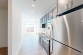 Located at 9420 Grand Blvd in Upper Marlboro, MD, this well-designed one-bedroom, one-bathroom unit offers a clean, modern aesthetic throughout its efficiently laid-out single floor. Light wood-tone flooring flows seamlessly across all rooms, complementing the crisp white walls and recessed lighting that brighten every corner.

The galley-style kitchen is outfitted with slate-gray shaker cabinetry extending to the ceiling for ample storage, white quartz countertops, a white subway tile backsplash, and a full suite of stainless steel appliances including a refrigerator, range, microwave, and dishwasher. The kitchen opens directly into the living area, which is anchored by a wall of oversized windows that flood the space with natural light and frame views of the surrounding tree line.

The bedroom is a calm, light-filled retreat featuring its own large window with outdoor views and access to a generously sized closet with built-in shelving. A dedicated laundry area and additional closet space add practical storage solutions throughout. The bathroom features a soaking tub with a full subway tile surround, a gray vanity with a quartz countertop, and the same warm wood-tone flooring found throughout the unit. A hallway connects all areas cohesively, completing this thoughtfully designed residence.
