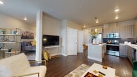This single-floor residence is designed with a contemporary aesthetic, combining clean lines, neutral tones, and high-quality finishes to create a cohesive and functional living environment. The open-concept layout seamlessly connects the kitchen, dining, and living areas, promoting an airy, connected feel throughout the space.

The kitchen is a standout feature, showcasing light wood-grain flat-front cabinetry, a dark subway tile backsplash, and a full suite of stainless steel appliances, including a French door refrigerator, range with microwave, and dishwasher. A central island with a white quartz countertop doubles as a breakfast bar with seating, making it ideal for both cooking and casual dining. A pendant light above the island adds a refined touch.

The living area offers generous space for entertaining, featuring dark hardwood-style flooring, recessed lighting, and large windows that invite natural light. The bedroom is carpeted for comfort, with windows providing additional natural light and a door that appears to lead to a private exterior access point.

The bathroom continues the modern theme with wood-grain vanity cabinetry, a white countertop, undermount sink, and brushed nickel fixtures. Throughout, the consistent use of warm wood tones, white surfaces, and gold accents creates a polished, welcoming ambiance.