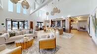 This expansive 3,320 square foot property in Fort Myers, Florida, showcases a contemporary single-story design with an emphasis on open, communal spaces. The interior is characterized by soaring ceilings and abundant natural light streaming through large windows, creating a bright and airy ambiance throughout.

The main living area features a seamless blend of lounge, dining, and kitchen spaces, ideal for both relaxation and entertainment. A striking architectural element is the vaulted ceiling with exposed beams, complemented by stylish pendant lighting. The decor combines modern and natural elements, with a neutral color palette accented by pops of color in the furnishings and artwork.

Multiple seating areas are thoughtfully arranged, including a plush green banquette and various lounge chairs, offering diverse spaces for socializing or quiet reflection. A well-appointed bar area with illuminated shelving adds to the property's entertainment potential.

The property boasts high-end finishes throughout, from the sleek light fixtures to the carefully curated decorative elements. Wood-look flooring unifies the space, while area rugs define individual zones within the open plan. Large-format artwork and carefully placed plants contribute to the sophisticated yet welcoming atmosphere.

This versatile space appears designed to accommodate various functions, potentially serving as a clubhouse or common area in a larger residential or hospitality complex. Its layout and amenities make it suitable for hosting events, providing workspace, or simply offering residents a luxurious environment for daily living.