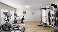 Located in Clemmons, NC, this dedicated exercise room offers a compact yet efficiently organized fitness space designed to support a comprehensive workout routine. The room features hardwood-style flooring throughout, neutral light gray walls, and a textured ceiling with flush-mount lighting that keeps the space bright and functional.

Natural light filters in through multiple windows fitted with white horizontal blinds, lending a clean, airy feel to the environment. The room is outfitted with an impressive array of fitness equipment, including a treadmill, an elliptical trainer, two stationary bikes, and a multi-function cable machine system, providing options for both cardio and strength training. A full dumbbell rack with a wide range of weights lines one wall, further enhancing the versatility of the space.

A wall-mounted electrical panel and a fire extinguisher near the exterior door reflect practical safety considerations. The exterior door provides direct outdoor access, adding convenience to the layout. The overall design is straightforward and purpose-driven, prioritizing function and ease of movement. This exercise room is well-suited for a varied fitness regimen, offering equipment variety rarely found in a space of this scale.