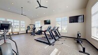 Located at 729 Crescent Woods Dr in Gahanna, Ohio, this dedicated fitness center offers a comprehensive workout environment designed to accommodate a wide range of exercise needs. The single-floor space is characterized by soaring vaulted ceilings that create an open, airy atmosphere, complemented by large, white-trimmed windows fitted with blinds that flood the room with abundant natural light while offering views of the surrounding landscape.

The durable speckled epoxy flooring throughout provides both a clean aesthetic and a practical surface suited for high-traffic fitness use. Overhead ceiling fans and recessed lighting ensure a comfortable environment during any workout. Wall-mounted flat-screen televisions are positioned throughout the space for entertainment while exercising.

The fitness center is thoroughly equipped for a full-body workout. Cardio offerings include multiple treadmills, elliptical machines, a stair climber, and stationary bikes. Strength training is well represented with a cable machine, adjustable weight benches, a comprehensive dumbbell rack, medicine balls, and resistance training accessories. A large mirror along one wall enhances the sense of space and allows for form monitoring during exercise. A wooden bench provides a convenient rest area. The clean, modern design and well-curated equipment selection make this fitness center a standout amenity.